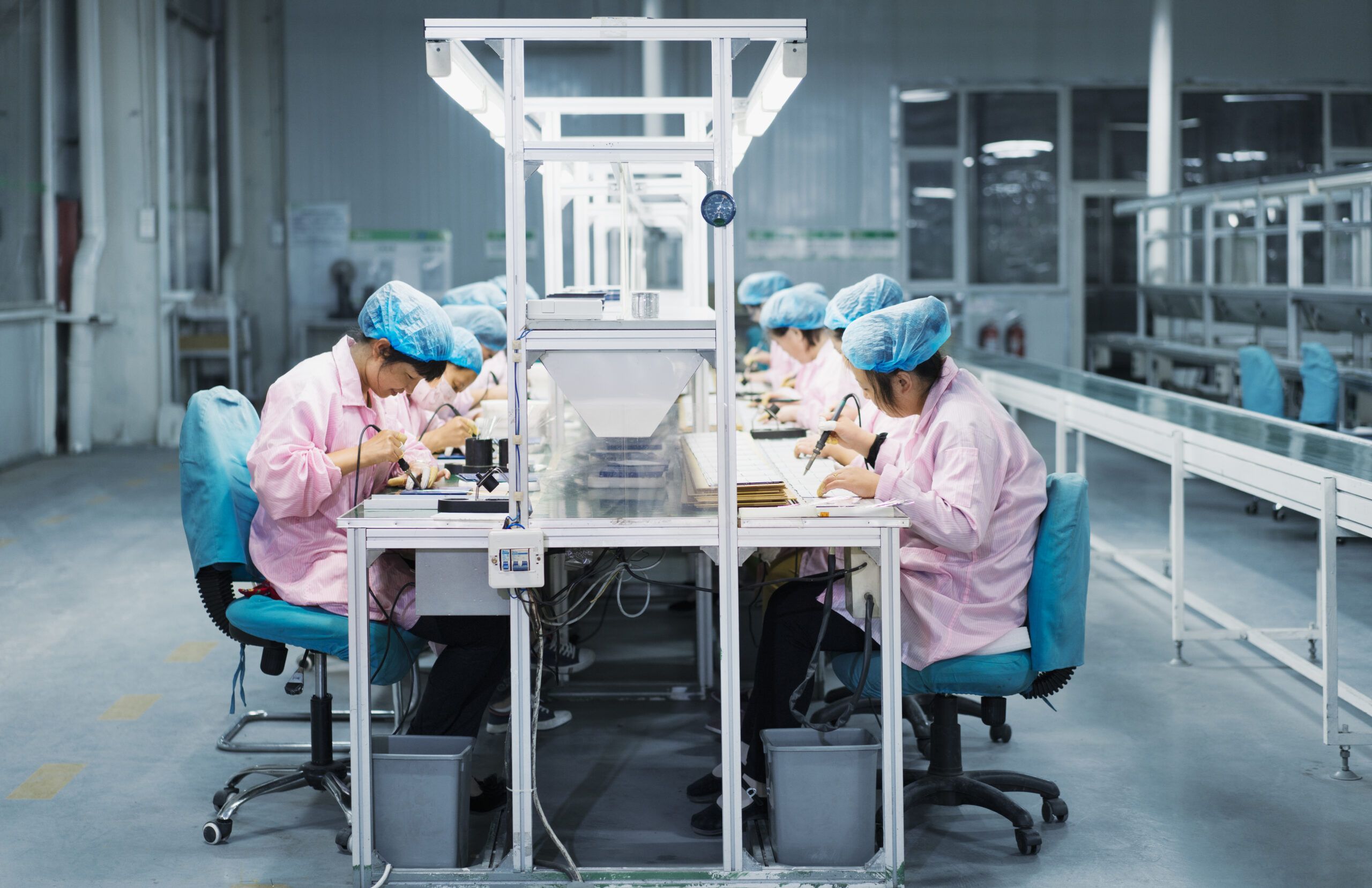 Workers in hairnets at assembly workstations in a solar panel factory